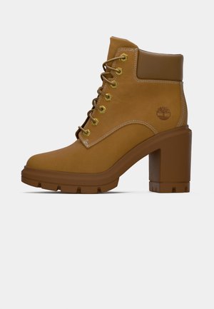 Tan leren veterschoenen tot de enkel met gouden oogjes, gewatteerde kraag, chunky blokhak en een merklogo op de zijkant.