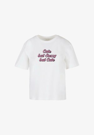 Fehér pamut póló, rózsaszín írott felirattal, amely így szól: "Cuki, de Szemtelen, de Cuki." Rövid ujjú, laza fazonú.