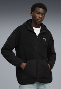 Schwarze Zip-Hoodie mit Fleece-Oberfläche und Baumwollärmel. Verfügt über eine Kängurutasche und das weiße Puma-Logo auf der Brust.