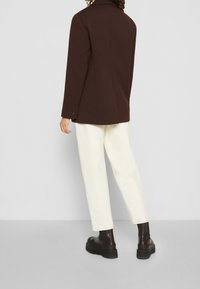 Blazer marrone con una vestibilità su misura, tessuto texturizzato e chiusura a un bottone. Abbinato a pantaloni bianchi e stivali robusti neri alla caviglia.