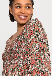 Vestido floral com corpete franzido, apresentando um padrão vibrante de flores vermelhas, brancas e verdes sobre um fundo preto. Mangas longas e volumosas.
