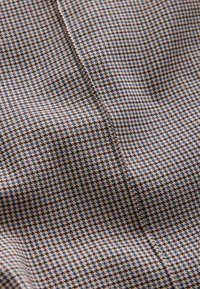 Pruun ja sinine houndstooth mustriga kangas, millel on tekstuuriga viimistlus, sile kude ja õrn sära.