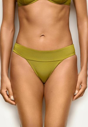 Kobieta w oliwkowych dołach od bikini z szerokim pasem, widoczna od talii do górnej części ud na neutralnym tle.