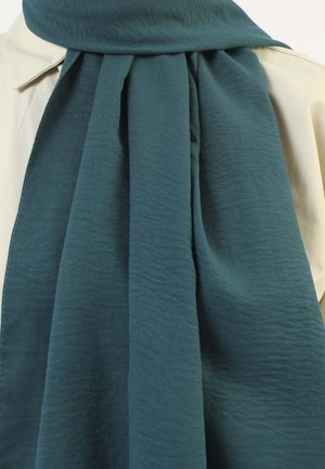 Teal, textured scarf draped around a light-colored shirt, featuring soft, flowing fabric and a smooth finish. No visible patterns or hardware.