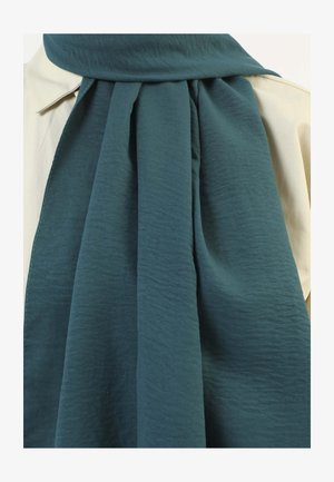 Teal, textured scarf draped around a light-colored shirt, featuring soft, flowing fabric and a smooth finish. No visible patterns or hardware.