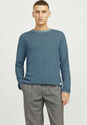Blauwe gebreide trui met een gestructureerde stof, ronde halslijn en geribbelde manchetten, gecombineerd met grijze, relaxed fit broek.