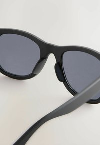Lunettes de soleil noires avec verres foncés et finition mate élégante. Comprend des branches courbées et des coussinets de nez pour plus de confort. Présente un design moderne.
