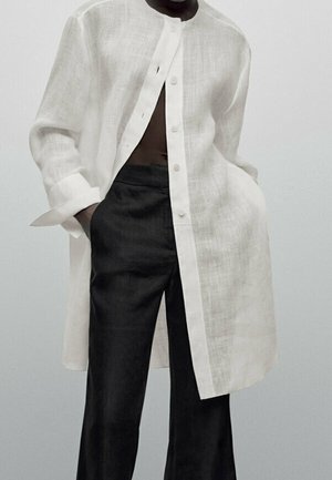 Weißes Leinenhemd mit Mandarinkragen, Knöpfen vorne und langen Ärmeln. Kombiniert mit dunklen, locker sitzenden Hosen. Minimalistisches Design.