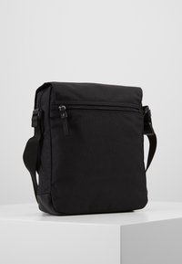 Borsa a tracolla nera realizzata in tessuto resistente. Presenta un lembo con una tasca con zip e una tracolla regolabile.