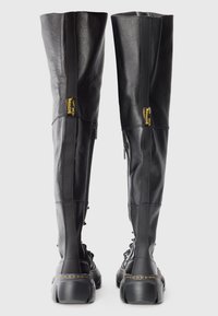 Black leather over-the-knee boots with a textured finish, featuring a side zipper, chunky sole, and yellow branding detail.