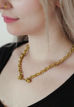 Nahaufnahme einer Frau, die eine grobe goldene Gliederkette und einen goldenen Nasenring trägt, bekleidet mit einem schwarzen Oberteil.
