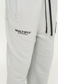 Pantalones de chándal gris claro fabricados en una mezcla de algodón. Presentan una cintura con cordón, bolsillos laterales y el logo "MULTIPLY APPAREL" en negro.