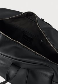 Čierna kožená taška s otvoreným zipsom. Vo vnútri je hladká látková podšívka a vrecko na zips. Pevné rukoväte a minimalistický dizajn.