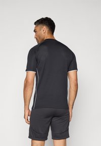 Black athletic shirt with short sleeves featuring white accents, paired with dark shorts. Material appears lightweight and textured.