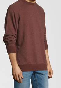 Sudadera granate con tejido texturizado, mangas raglán, puños y dobladillo de canalé, corte relajado, combinada con jeans de color azul claro.