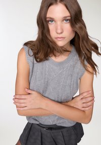 Top senza maniche grigio lavorato a maglia con design a trecce testurizzate, scollatura rotonda, abbinato a una gonna a quadri nera con vita aderente.