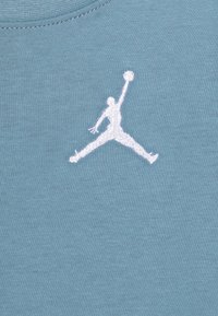 Jasnoniebieska bawełniana koszulka z białym haftowanym logo Jumpman umieszczonym centralnie, o miękkiej, gładkiej fakturze.