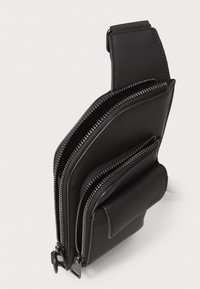 Zwarte gestructureerde tas met meerdere ritscompartimenten, gemaakt van een glad materiaal met horizontale stiksels en een platte zijzak.