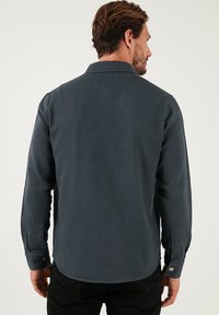Camicia blu scuro realizzata in tessuto testurizzato con colletto a punta, maniche lunghe, polsini con bottoni e orlo curvo. Design minimalista.