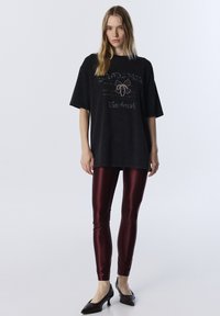 Czarna, oversize koszulka z cekinowym wzorem i napisem, w połączeniu z błyszczącymi bordowymi legginsami i czarnymi szpilkami. Prosty, nowoczesny wygląd.
