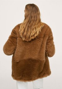 Brązowy płaszcz z futra ekologicznego o miękkiej, puszystej fakturze, z kapturem i luźnym krojem. Projekt obejmuje wzór z blokami kolorów na plecach.