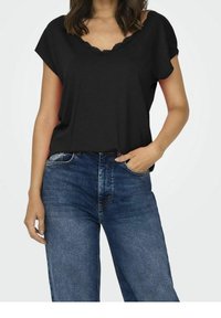 Top negro de manga corta con escote en V y detalles de encaje. Combinado con jeans de mezclilla azul, que destacan un ajuste relajado y un diseño clásico.