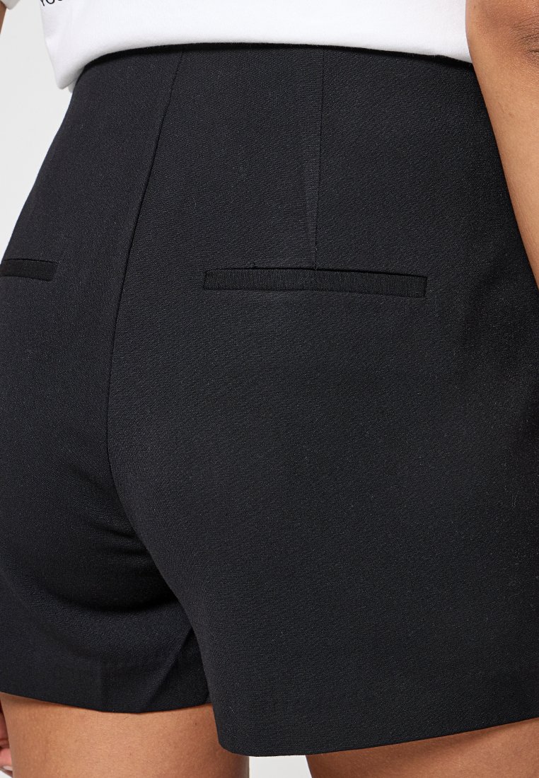 Pantalones cortos negros ajustados con una textura suave, diseño minimalista, dos bolsillos traseros y corte recto.