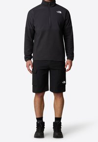 Black fleece pullover with quarter zip and The North Face logo, paired with black cargo shorts featuring pockets and logo accents.