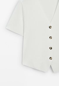 Blusa a maniche corte di un grigio chiaro con scollatura a V e sei bottoni rotondi lungo la parte anteriore, realizzata in un tessuto liscio e leggero.