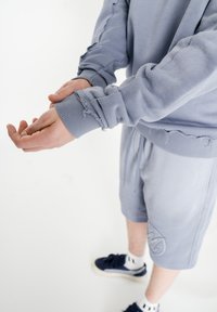 Svetlomodrá mikina s netriedenými okrajmi a rebrovanými manžetami, skombinovaná s nohavicami v rovnakom odtieni so značkovým logom. Hladká, mierne štruktúrovaná tkanina.