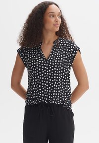Zwarte blouse met korte mouwen en een V-hals, met witte vierkante patronen, gemaakt van lichte stof, gecombineerd met zwarte broek met koord.