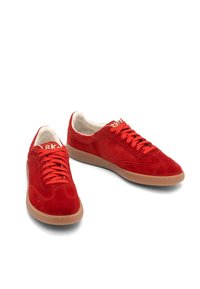 Czerwone zamszowe sneakersy o smukłym wyglądzie, z okrągłymi sznurówkami, kontrastującą gumową podeszwą i subtelnymi detalami szycia.