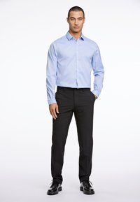 Camicia azzurra chiara a maniche lunghe con bottoni abbinata a pantaloni neri e scarpe eleganti nere. La camicia presenta un colletto a punta e un design aderente.