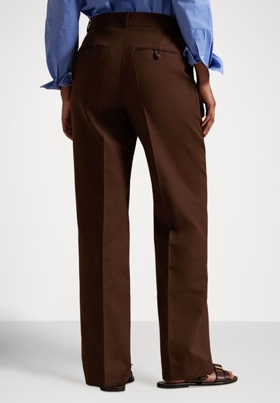Καφέ παντελόνι κομμένο και ραμμένο με ίσια γραμμή, δύο πίσω τσέπες και λεία υφή, συνδυασμένο με καφέ σανδάλια.