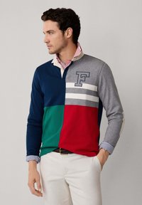 Langarm-Poloshirt mit Farbblöcken in Marineblau, Grün, Rot und Grau; vertikale Streifen; gesticktes "F"; Kragen mit einem kontrastierenden Hemd darunter.