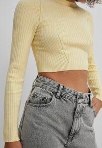 Haut court à manches longues en tricot côtelé jaune, associé à un jean gris déchiré taille haute. Présente une coupe ajustée et des détails subtils de coutures.