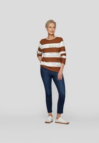 Braun und weiß gestreifter Pullover mit aufgedrucktem Text, kombiniert mit dunkelblauen Jeans und weißen Sneakers, im lässigen Schnitt und mit rundem Halsausschnitt.