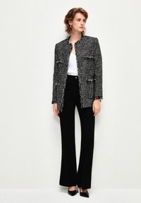 Černobílý tvídový sako s třepenými okraji, se dvěma našitými kapsami, nošené přes bílé tričko. V kombinaci s vysokým černým rozšířeným kalhotami a podpatky.