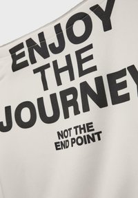 Tessuto bianco con grande testo nero che recita "GODITI IL VIAGGIO" sopra "NON IL PUNTO D'ARRIVO". Texture liscia, design semplice.