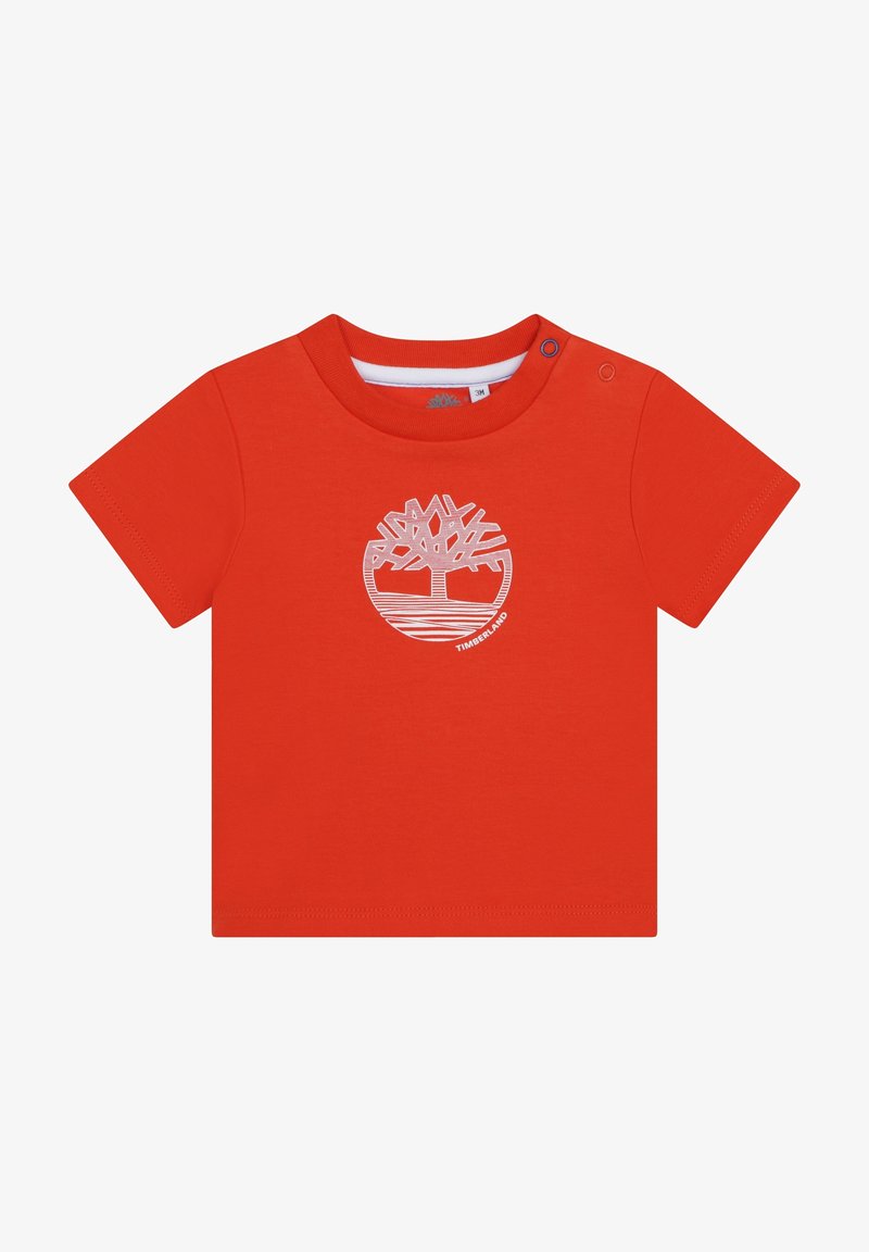 T-shirt en coton rouge à manches courtes avec un logo Timberland blanc en forme de cercle, présentant un motif d'arbre et des lignes horizontales en bas. Fermeture à boutons-pression.