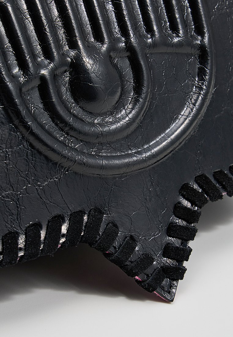 Gros plan sur un cuir noir texturé avec un motif incurvé en relief et une bordure en suède noir cousue le long du bord.