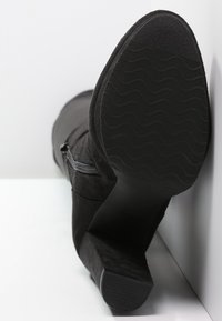 Stivaletto in suede nero con punta affusolata e silhouette elegante. Presenta una suola texturizzata e dettagli in cerniera argentata sul lato.