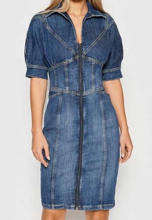 Kvinde iført en knælængde, tætsiddende denimkjole med korte, puffede ærmer og lynlås foran.