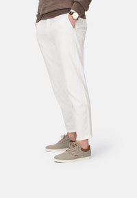 Leichte weiße Hosen mit Seitentaschen, kombiniert mit grauen Schuhen, die eine strukturierte Oberfläche und Akzente aus braunem Leder aufweisen.