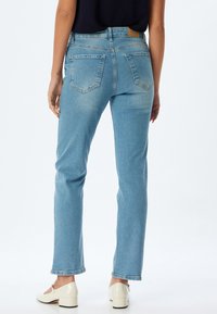 Jeans de mezclilla azul claro con un diseño de pierna recta, estilo de cinco bolsillos y una cintura de altura media. Terminados con un ligero desgastado y detalles de costura.