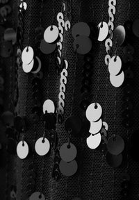 Tessuto nero adornato con paillettes alternate bianche e nere, caratterizzato da una forma circolare e una texture riflettente, attaccato da sottili fili.