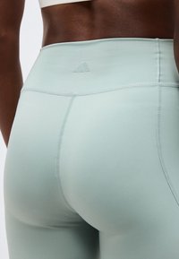 Κλείσιμο πλάνου ενός ατόμου που φοράει ελαφρώς γαλάζια κολάν με ψηλή μέση, με ορατές ραφές και ένα μικρό λογότυπο Adidas στη πίσω μέση.