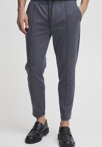 Jogging gris foncé en tissu doux, avec une taille élastique à cordon de serrage, des poches latérales et des jambes fuselées avec de subtils détails de couture.