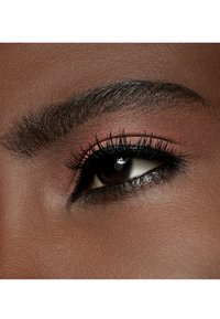 Close-up van een oog met donkere wimpers, een gedefinieerde wenkbrauw en zachte bruine oogschaduw. Gladde huidtextuur met een rijke teint.