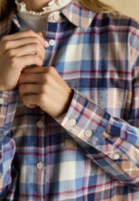 Button-up plaid shirt in blue, pink, and white; soft fabric with a relaxed fit. Features a collar and embroidered detailing on the cuff.